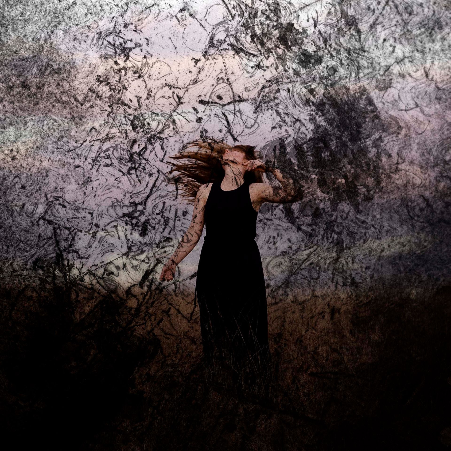 A woman in a black dress is standing in a field with her hair blowing in the wind