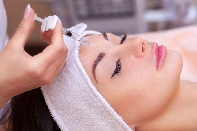 Person receiving an injection in the forehead while reclining, likely for a cosmetic procedure.