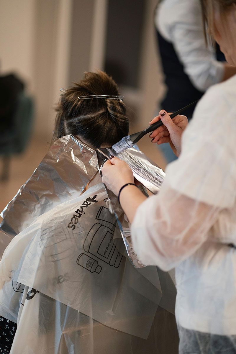 Hairdresser applying hair dye with a brush, using foil on a client's hair in a salon.