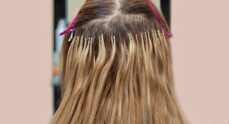 Blonde hair extensions attached to natural hair with metal clips, viewed from behind.