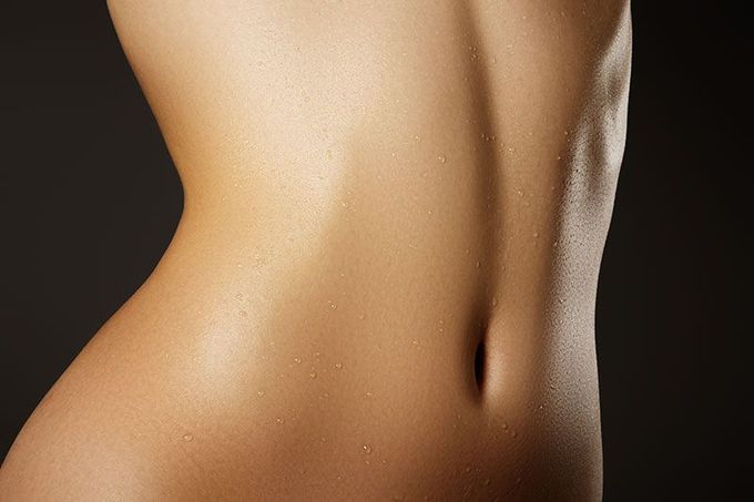 Close-up of a smooth, tan torso and back with a defined waist against a dark background.
