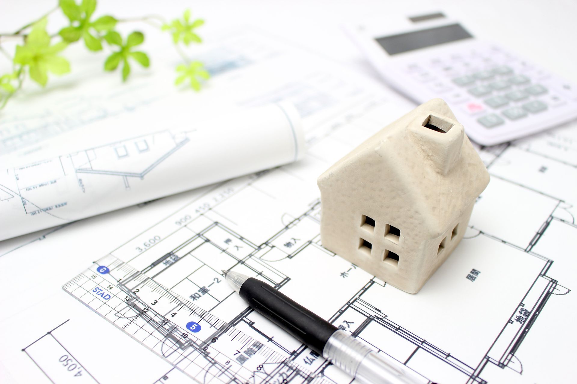 Un modello di casa è seduto sopra un progetto accanto a una penna e una calcolatrice.