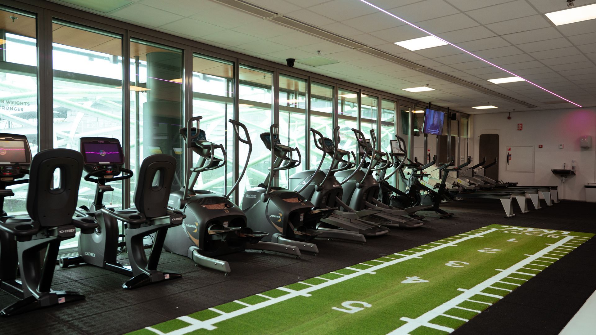 Een sportschool met veel fitnessapparatuur en groene verlichting.