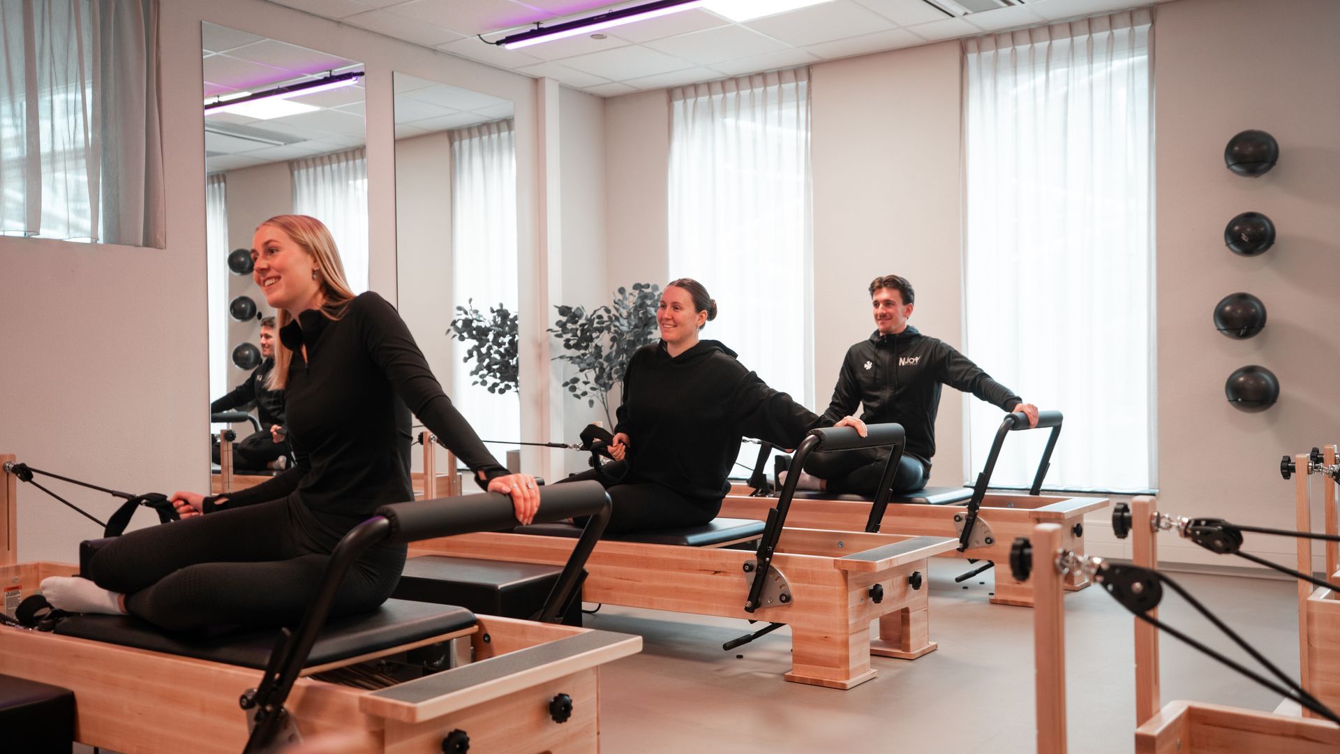 Mensen die oefeningen doen op pilatesapparaten in een lichte studio.