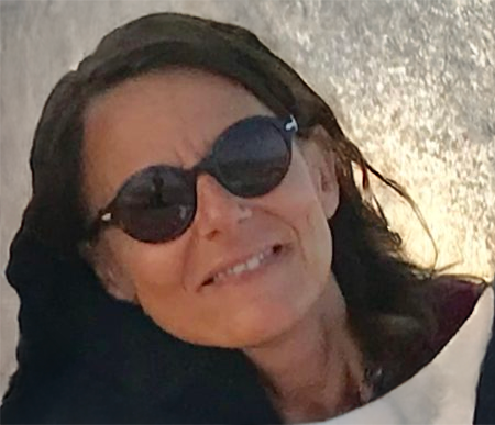 Femme aux cheveux noirs, portant des lunettes de soleil, souriant légèrement, à l'extérieur.
