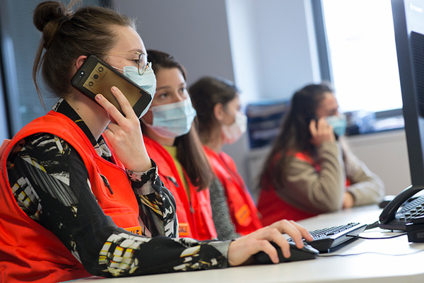 Des personnes vêtues de gilets rouges travaillent sur des ordinateurs dans un bureau, l'une d'elles est au téléphone.