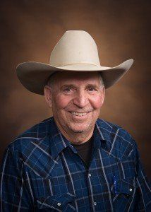 A man wearing a cowboy hat and a plaid shirt is smiling.