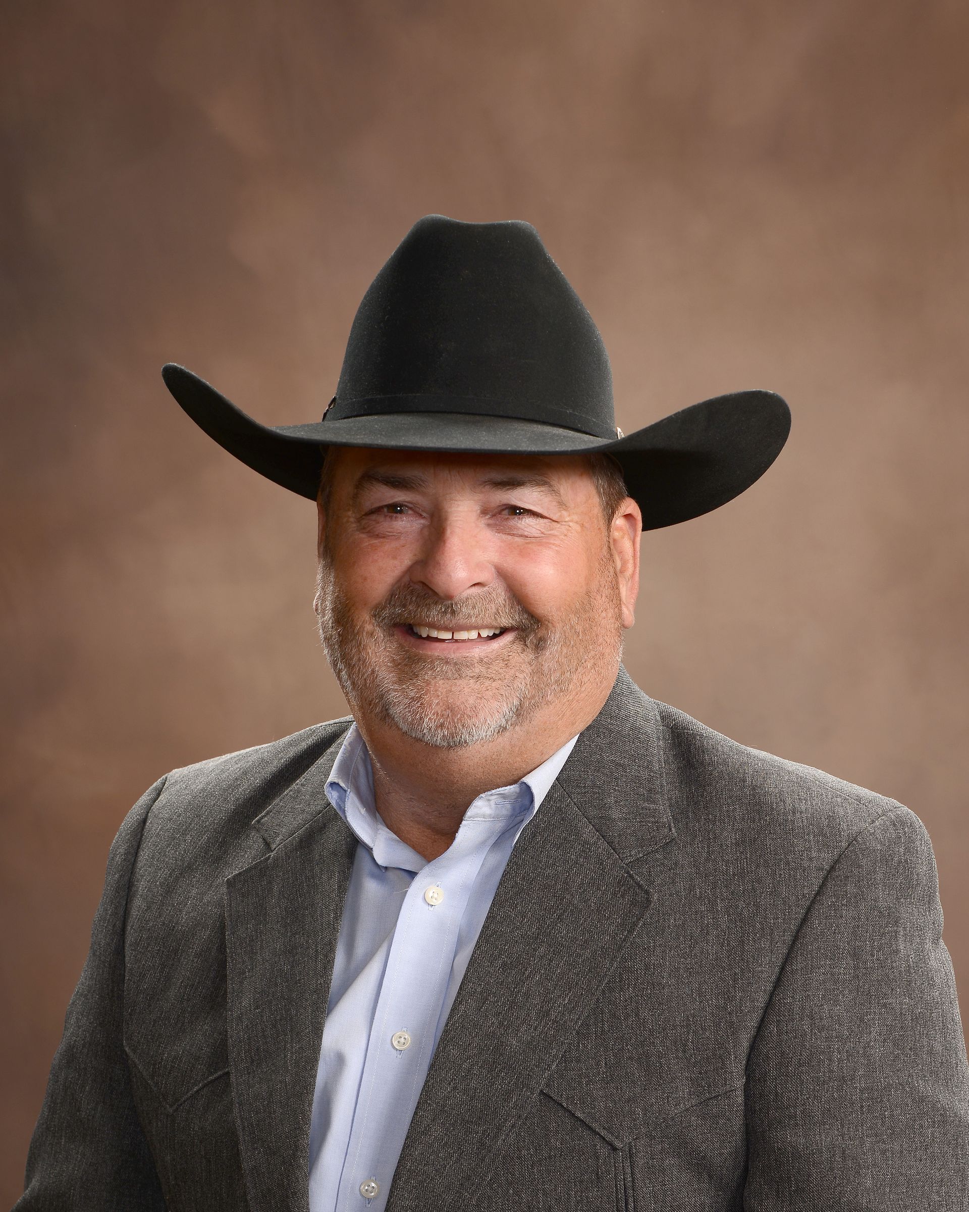 A man wearing a cowboy hat and a suit is smiling.