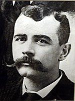 A black and white photo of a man with a mustache.