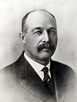 A black and white photo of a man with a mustache wearing a suit and tie.