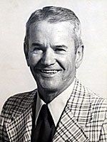 A man in a suit and tie is smiling in a black and white photo.