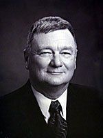 A man in a suit and tie is smiling in a black and white photo.