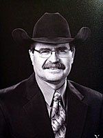 A man in a suit and tie is wearing a cowboy hat and glasses.