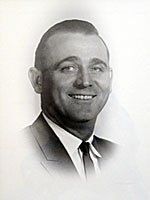 A black and white photo of a man in a suit and tie smiling.