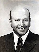 A man in a suit and tie is smiling in a black and white photo.