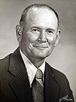 A man in a suit and tie is smiling in a black and white photo.