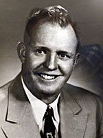 A man in a suit and tie is smiling in a black and white photo.