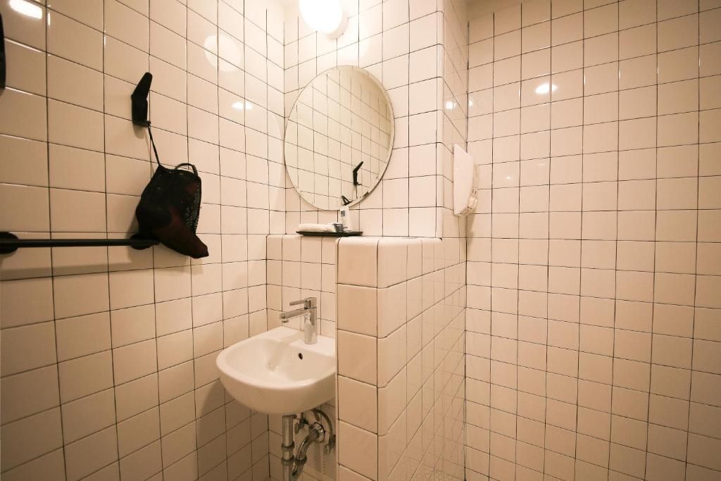 A bathroom with white tiles and a sink and mirror.