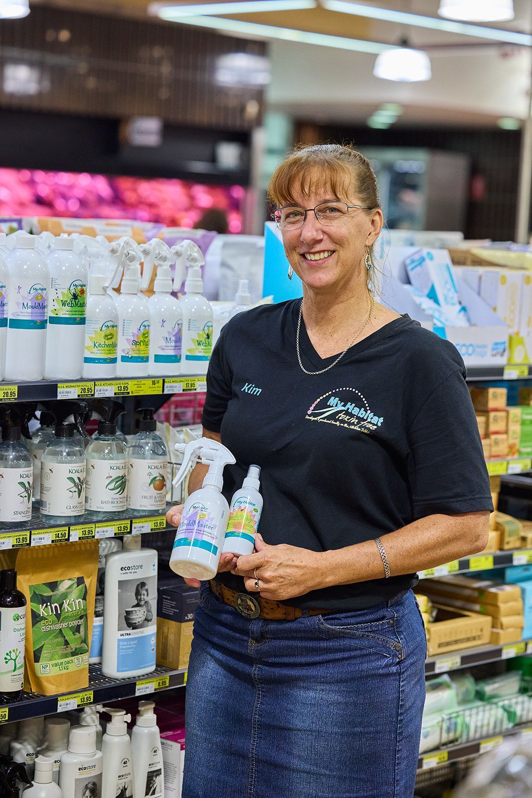 Smiling Woman in a Store Aisle Holding Bottles — My Habitat Products in Malanda, QLD