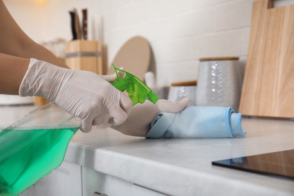 Person Wearing Gloves Sprays Cleaning Solution on A Kitchen Countertop — My Habitat Products in Cairns, QLD