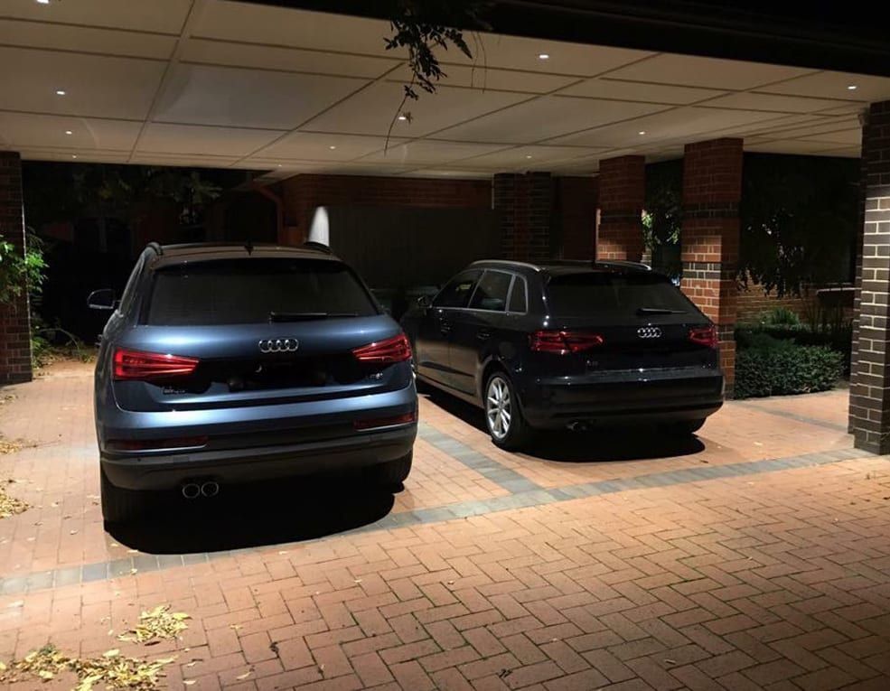 Two cars are parked in a driveway at night.