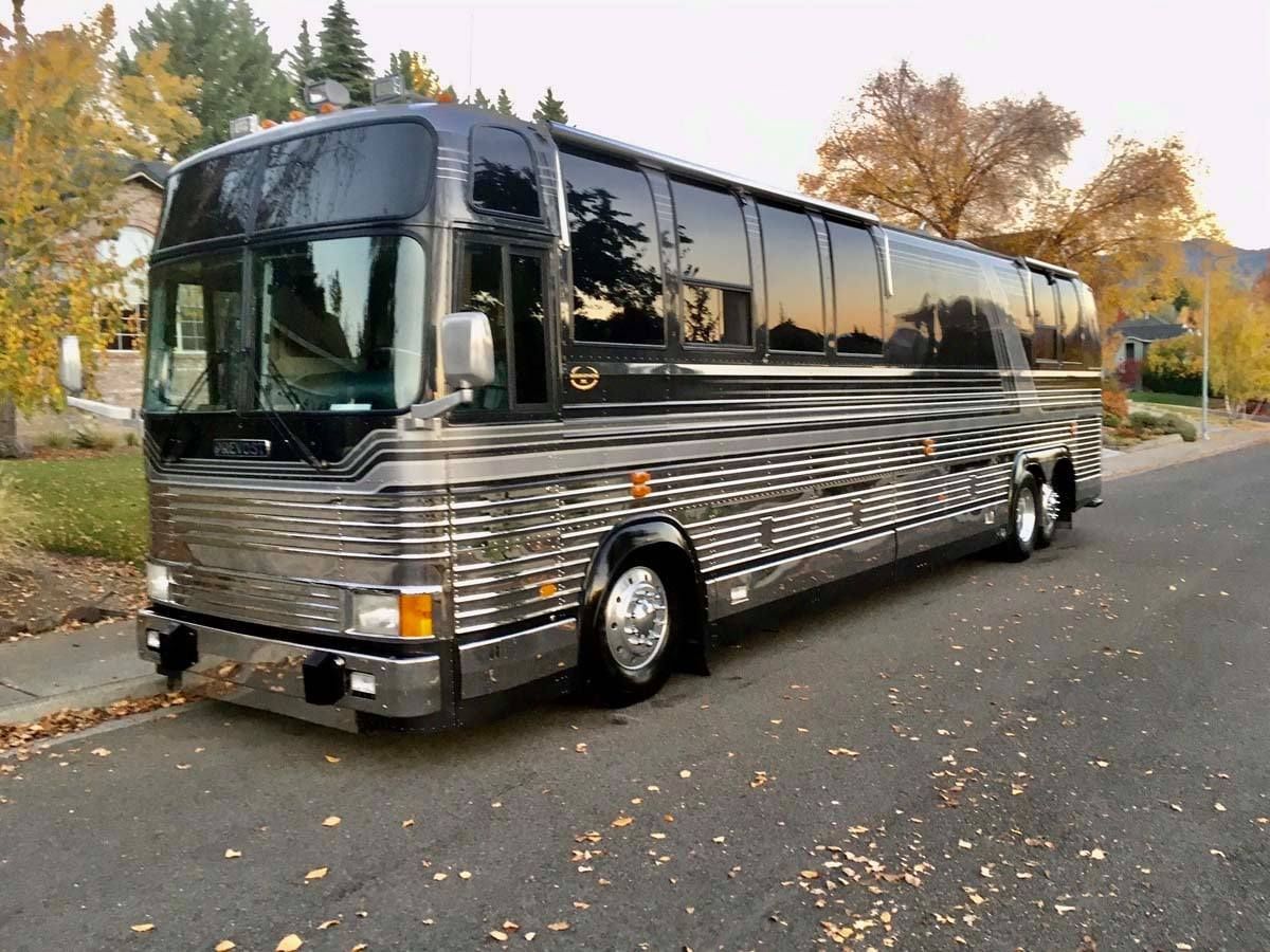 A silver Prevost motorcoach parked on a residential street during autumn.