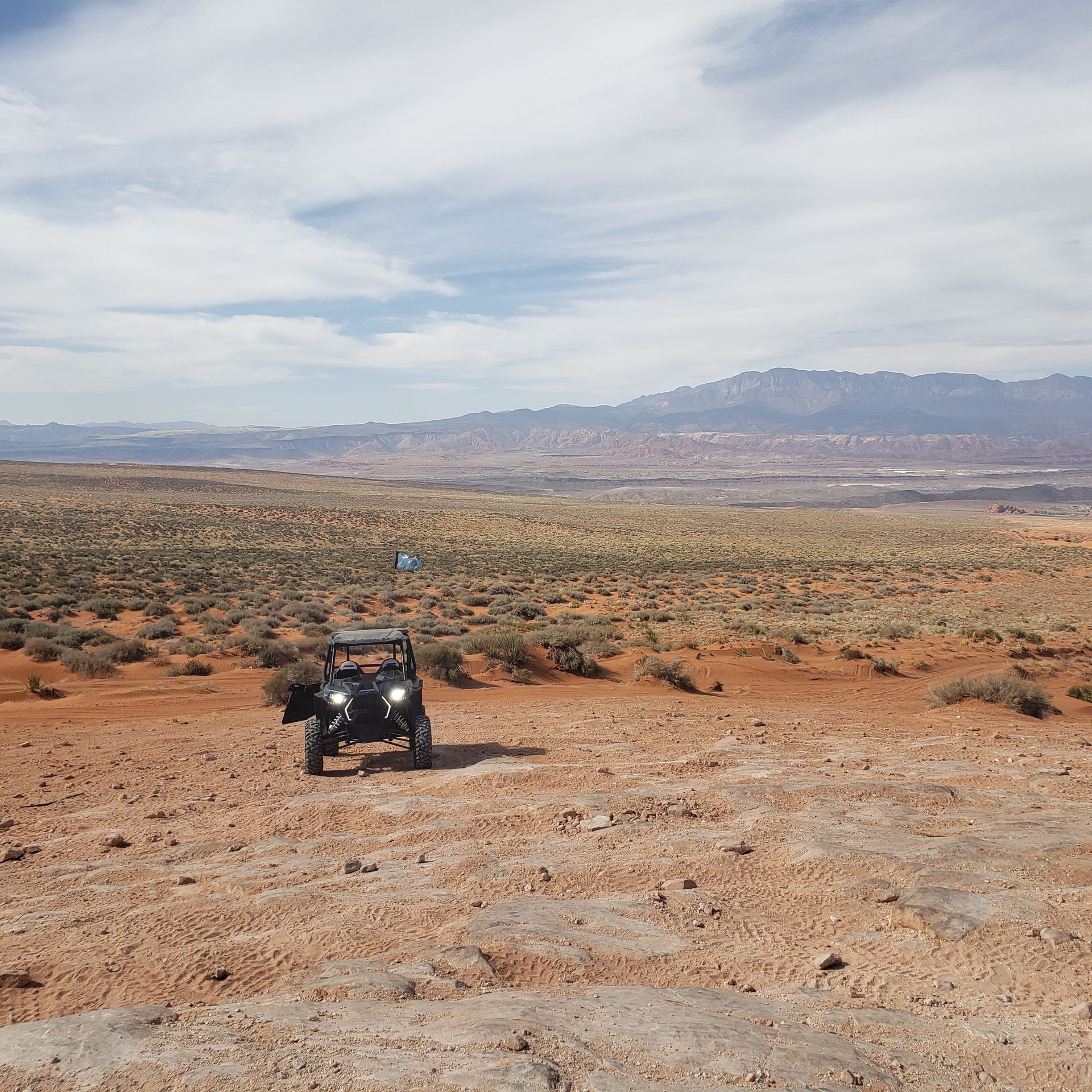 A black all-terrain vehicle sits on a reddish desert landscape with distant mountains under a cloudy sky.