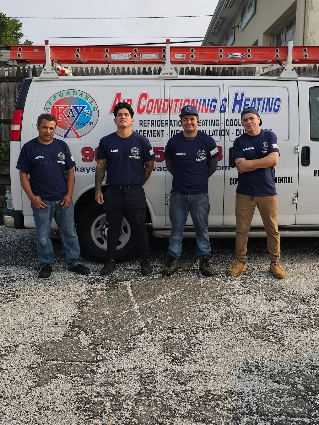 Four technicians wearing matching dark blue shirts stand in front of a white service van for an HVAC company.