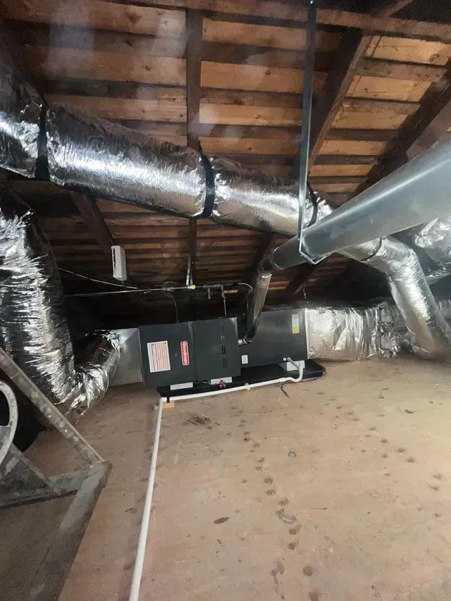 A horizontal HVAC unit with attached silver ductwork installed in a wooden attic space.
