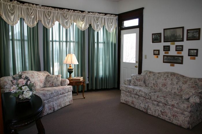 A cozy sitting room featuring two floral sofas, a lamp, a side table, and a gallery wall of framed photos on the right.