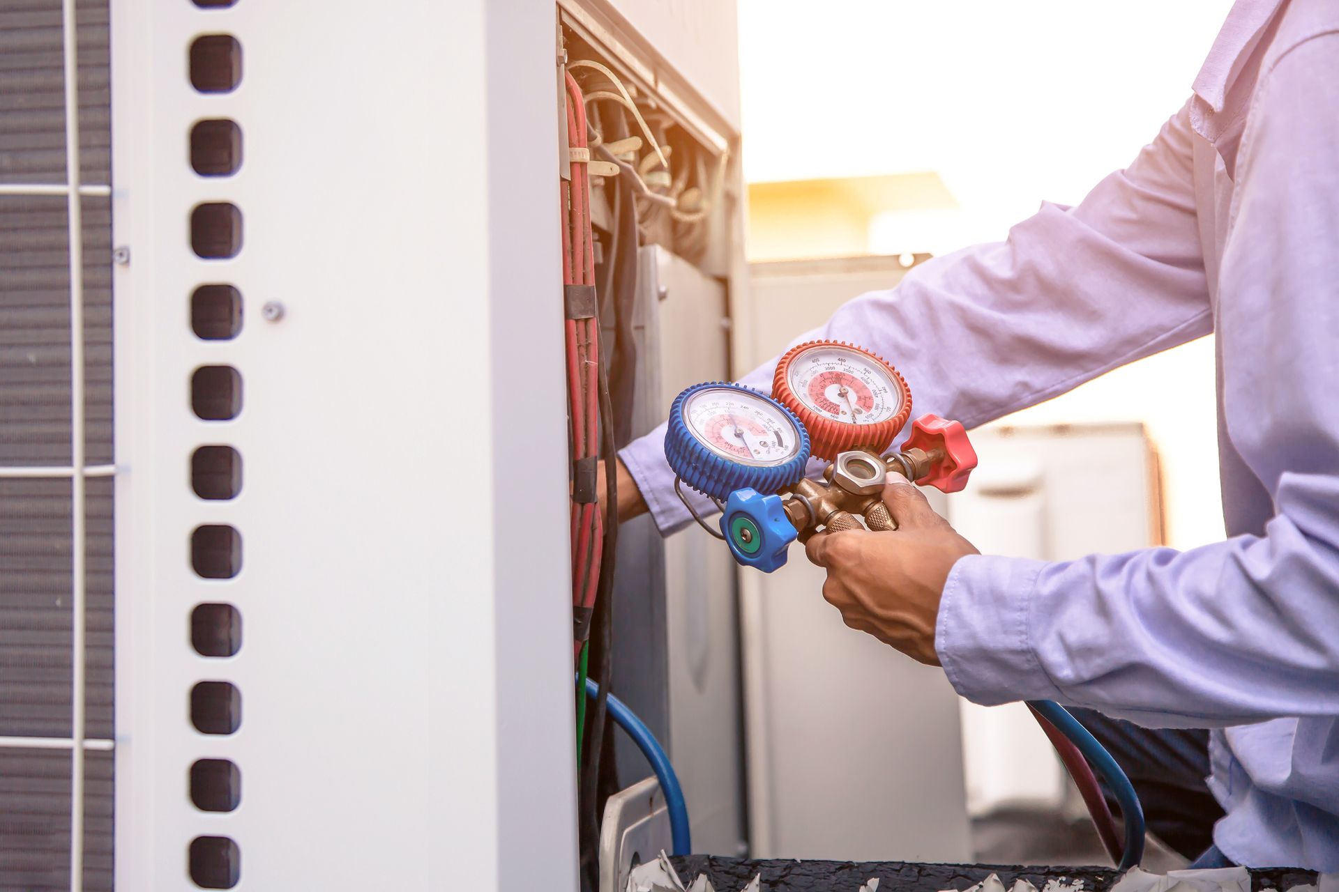 Technician connecting pressure gauges to an outdoor unit while performing commercial cooler repair. Technician connecting pressure gauges to an outdoor unit while performing commercial cooler repair.