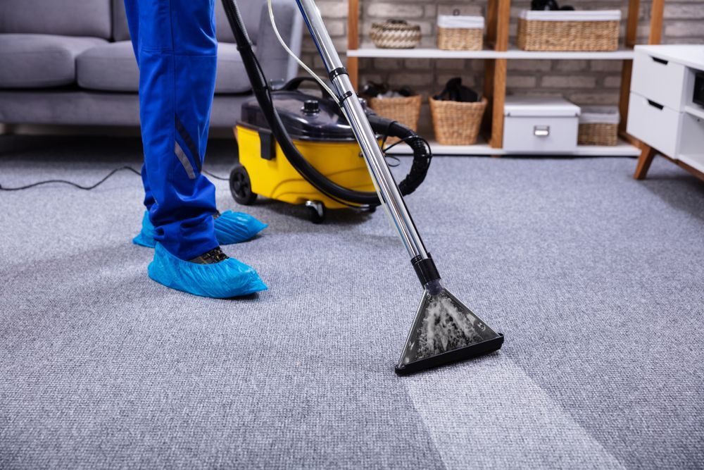 Person vacuuming a light gray carpet with a yellow and black machine, leaving a clean stripe.