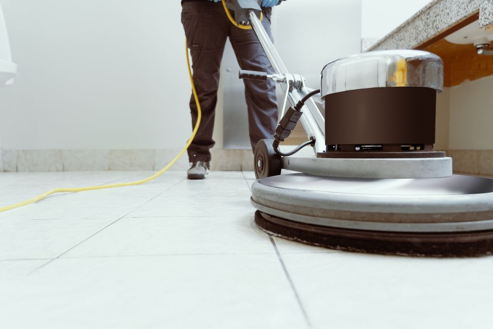 Person cleaning a tiled floor with an industrial floor buffer in a room.