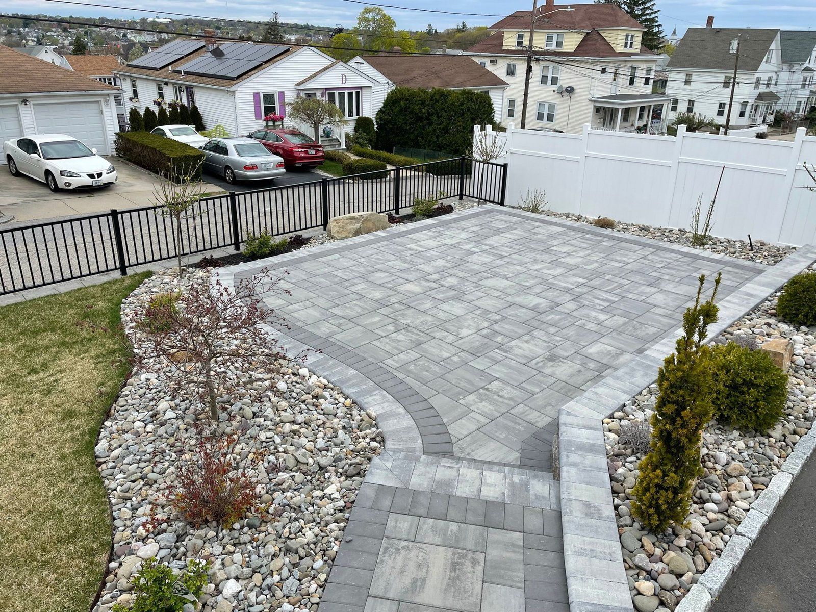 A paved stone patio with a retaining wall and surrounding gravel beds in a suburban backyard.