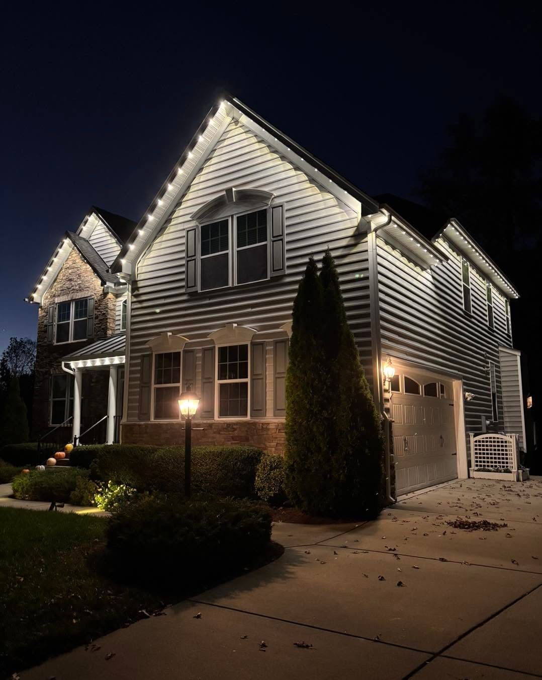 Two-story suburban house at night, outlined with bright white holiday lights along the roofline and garage.