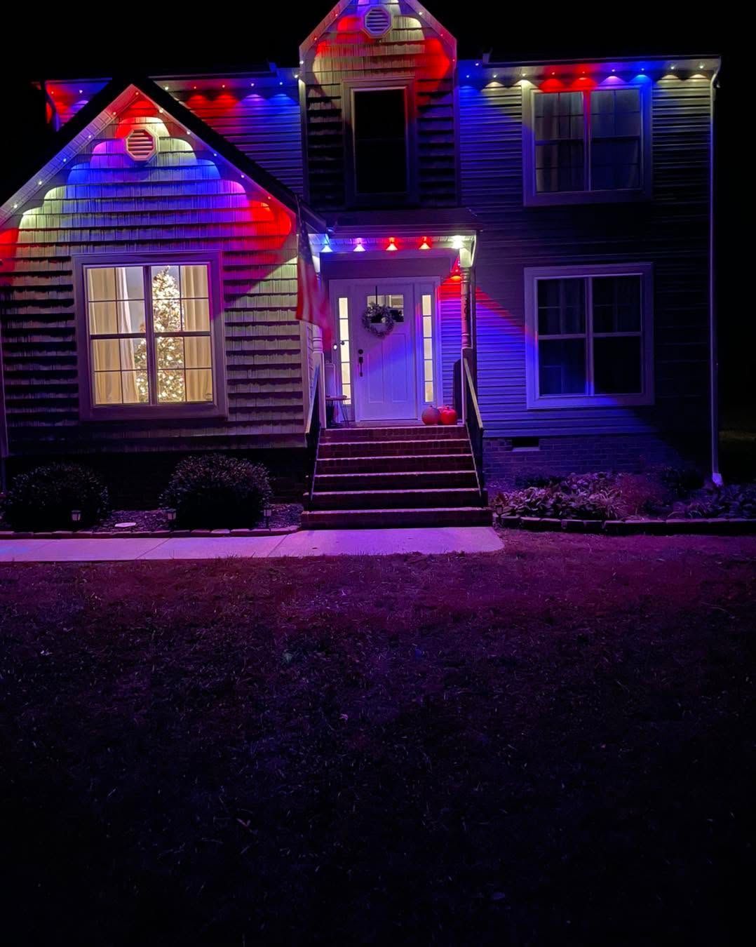 House decorated with red and blue holiday lights at night, glowing doorway and windows.