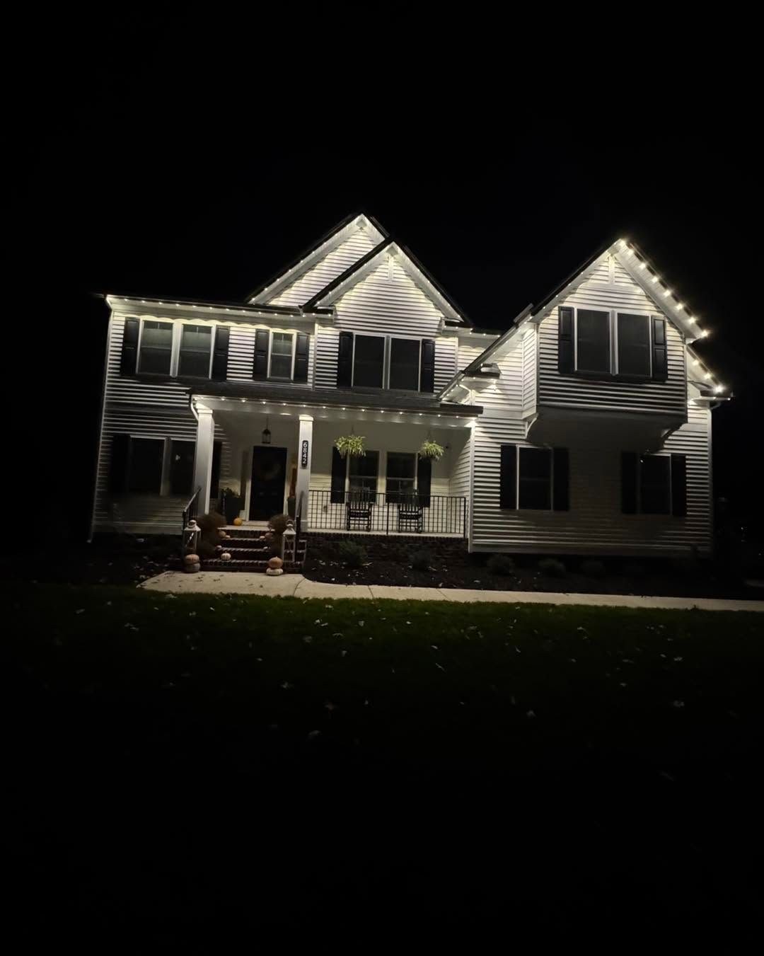 Two-story house at night outlined with bright white Christmas lights on the roof and windows