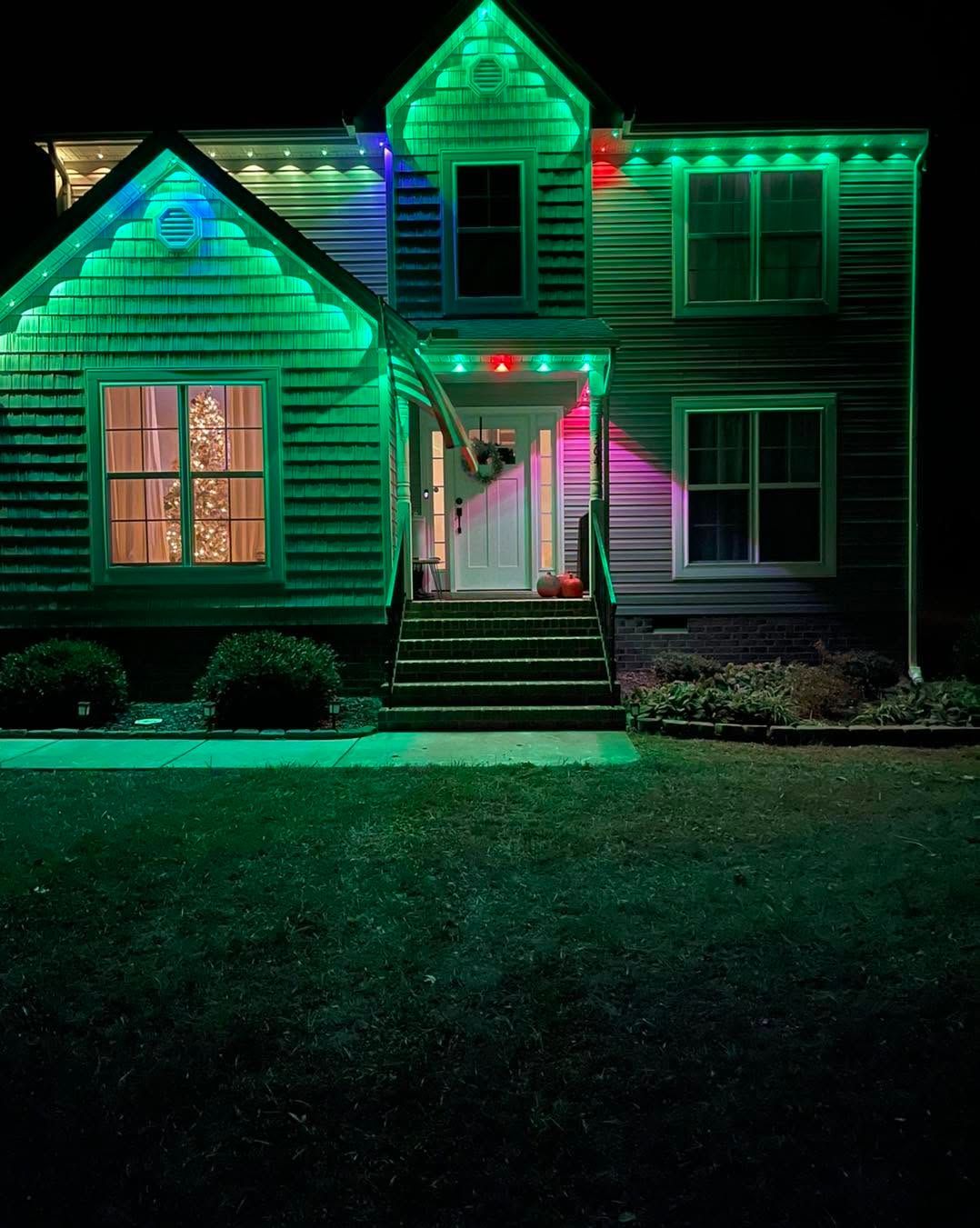House lit with green and red holiday lights at night, viewed from the front yard.