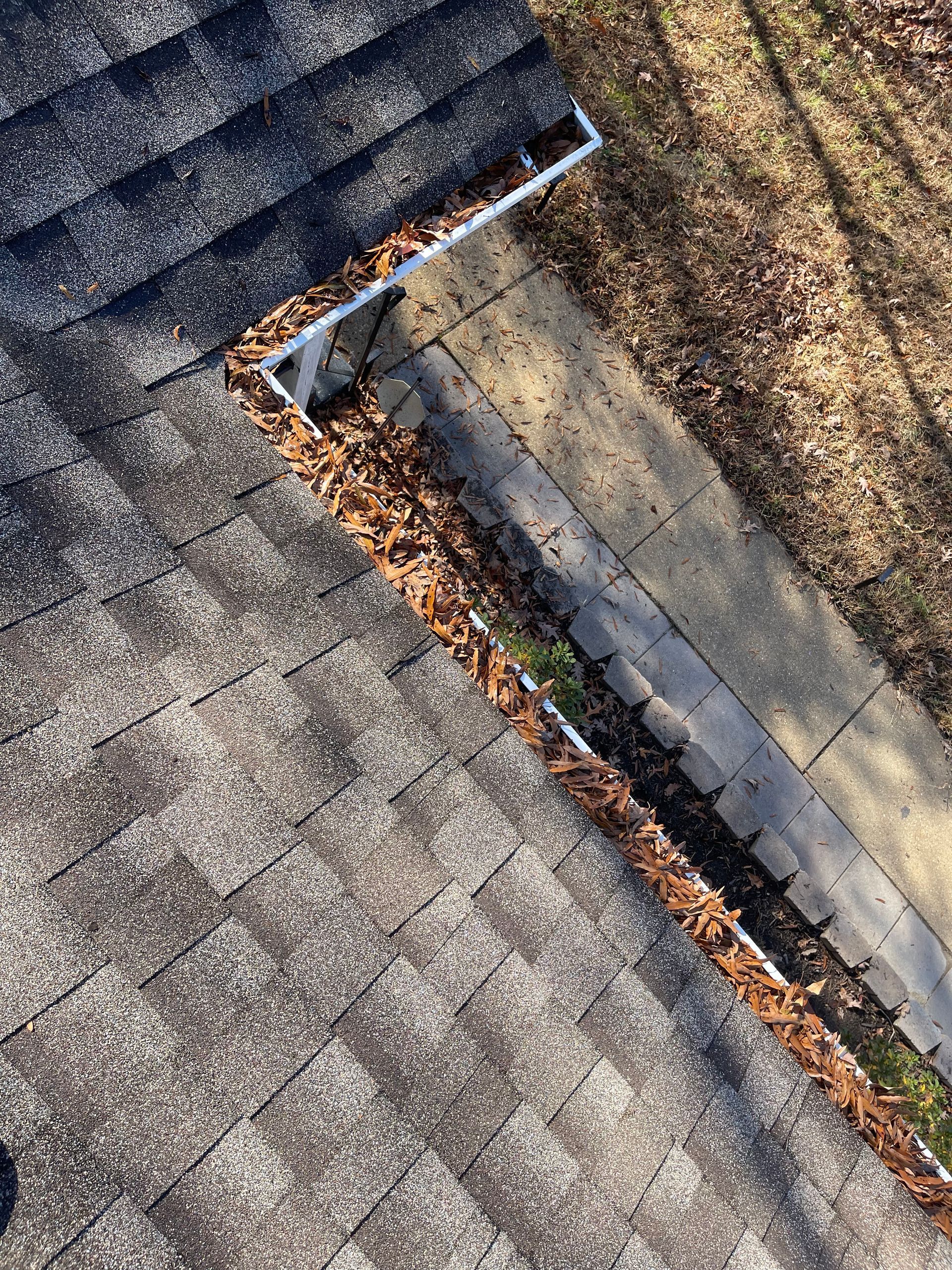 Close-up of a roof valley with gray shingles, a flashing strip, and autumn leaves along the edge