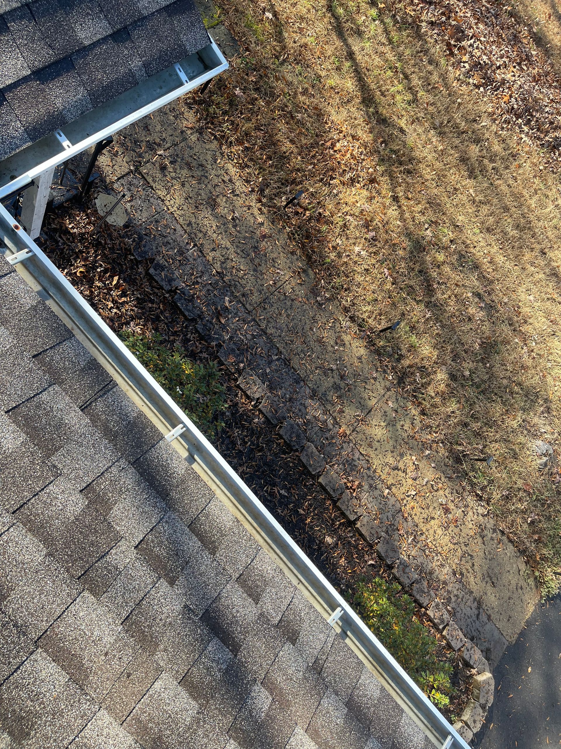 Roof gutter filled with debris beside a mossy, brown rooftop surface.