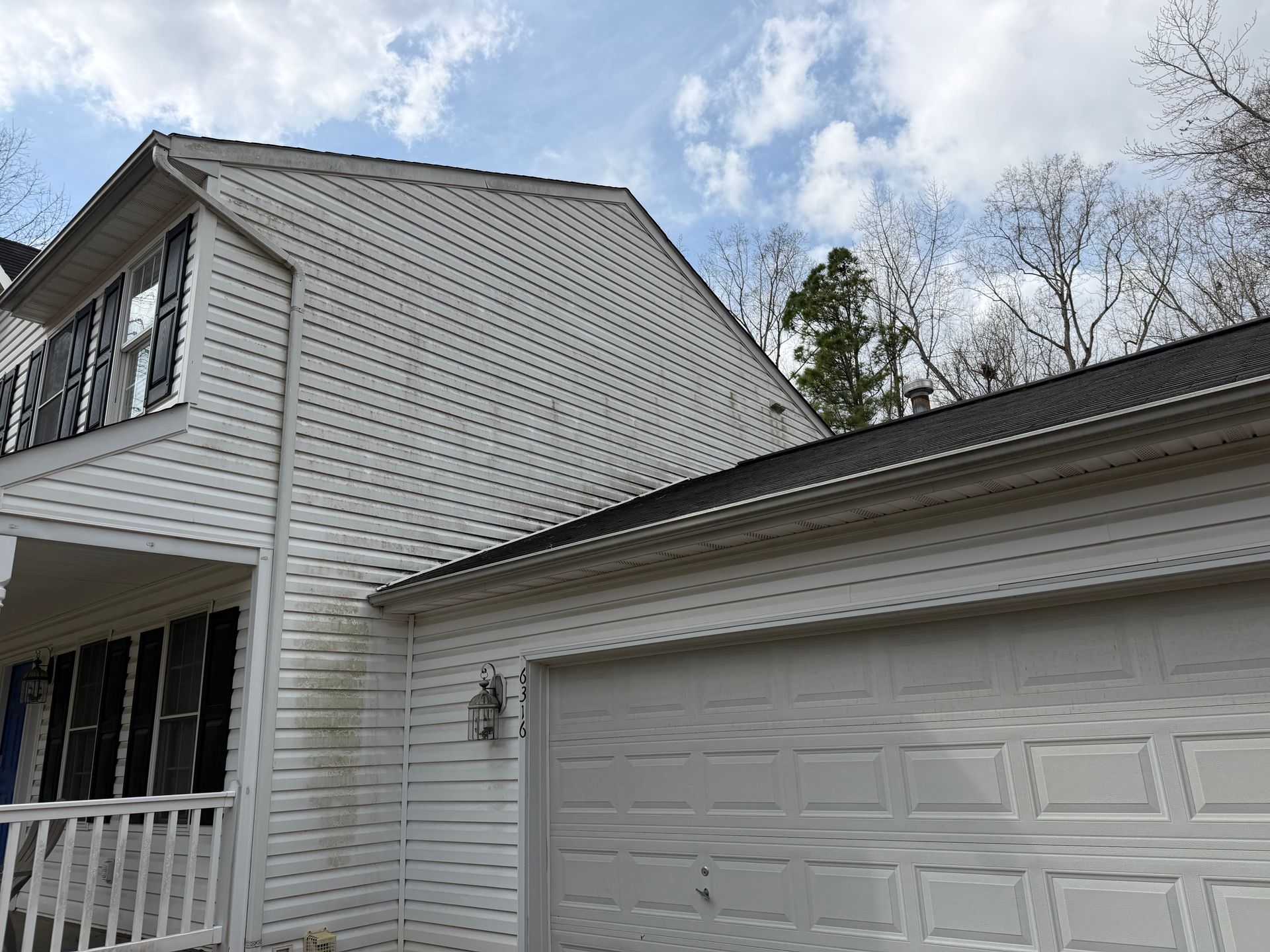 White house exterior with a two-car garage and porch under a partly cloudy sky