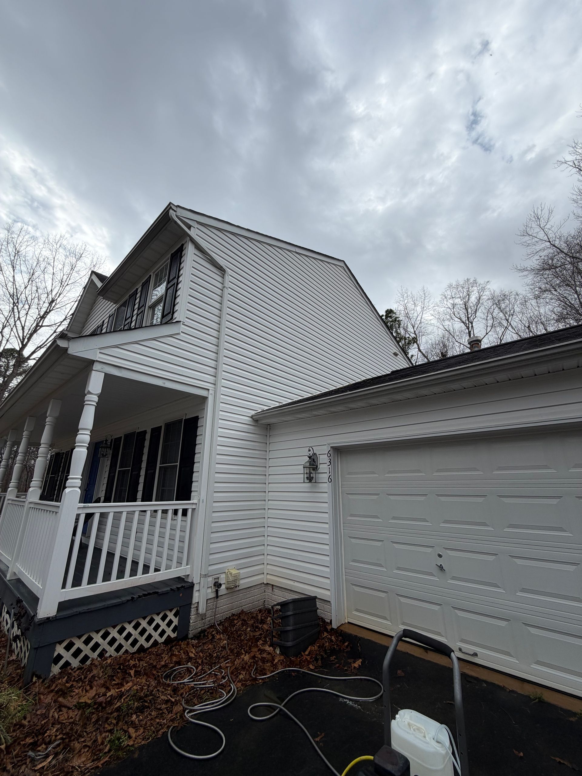 White two-story house with garage and porch under cloudy sky, with a wet driveway in front