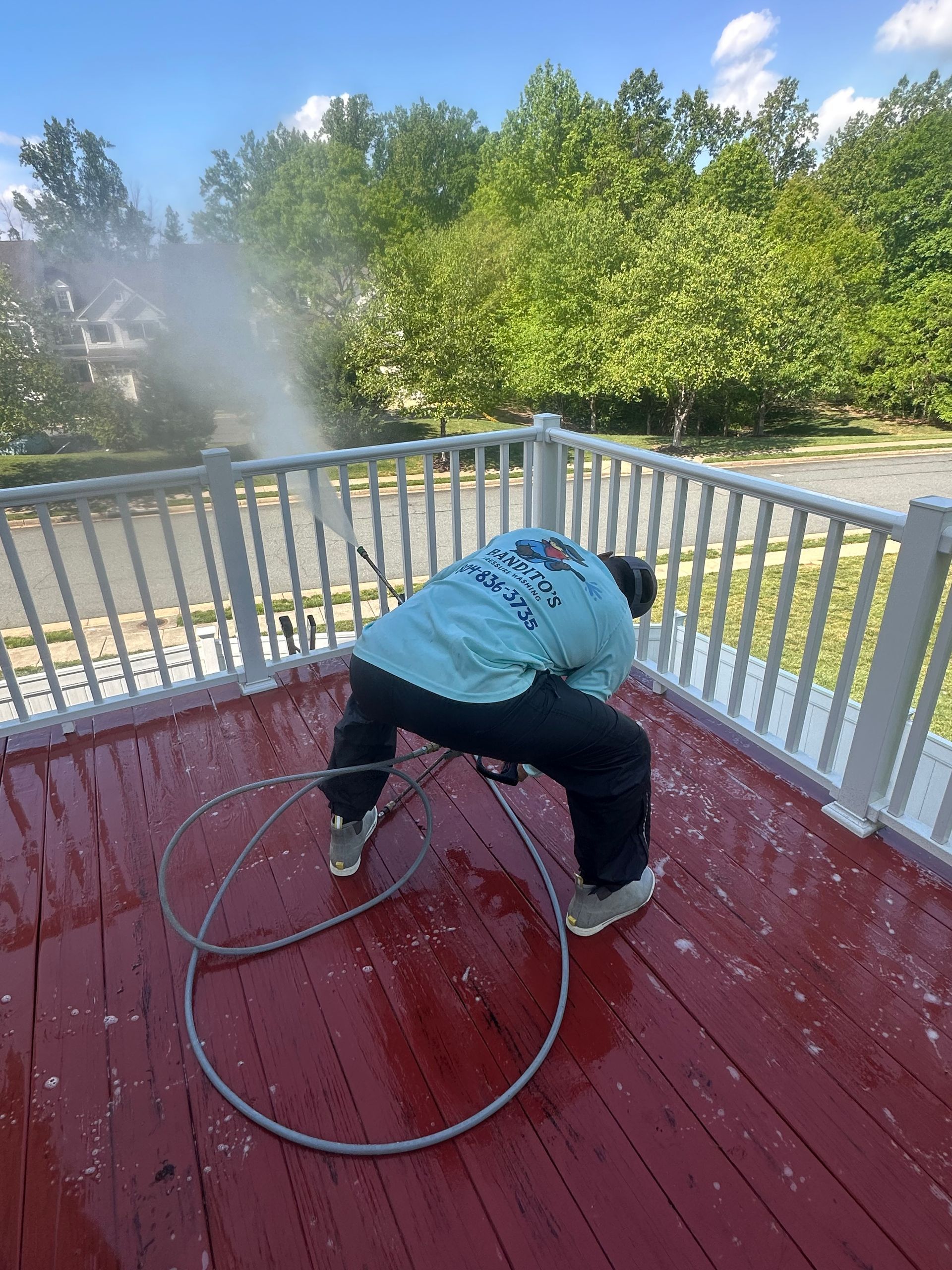 Person bending over on a red deck, holding a hose near a railing with trees and mist in the background