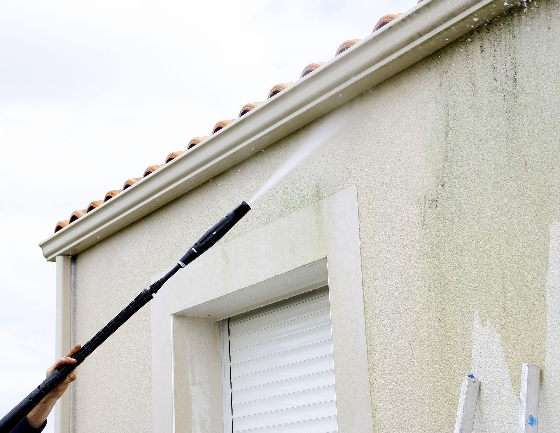 Person using a long paint roller to paint an exterior house wall near the roofline