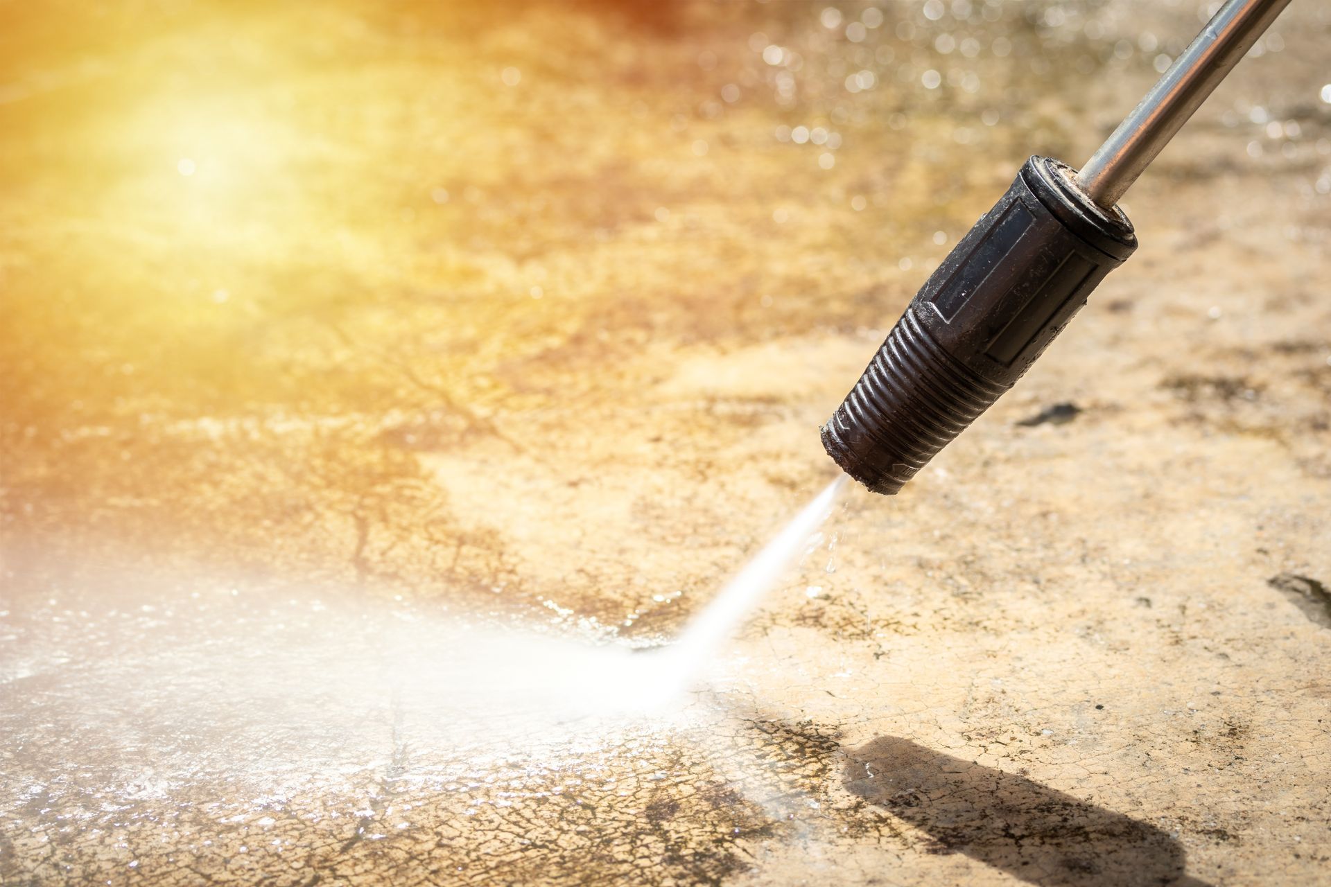 Pressure washer spraying water onto a dirty concrete surface, cleaning it under bright sunlight.