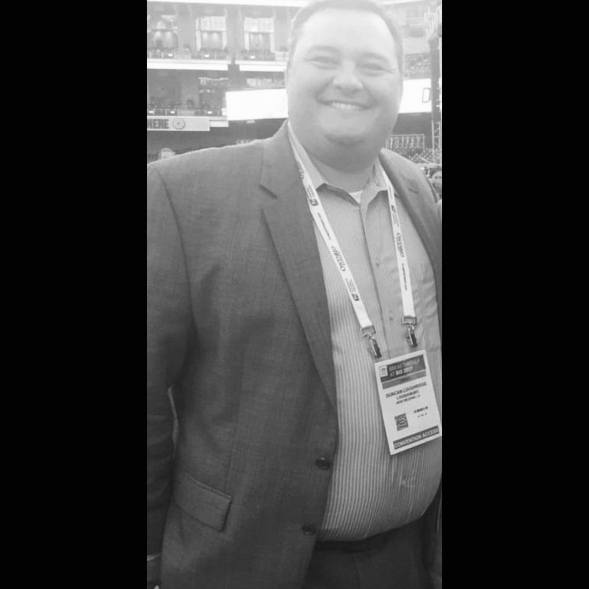 A man in a suit has a lanyard around his neck that has a name tag on it