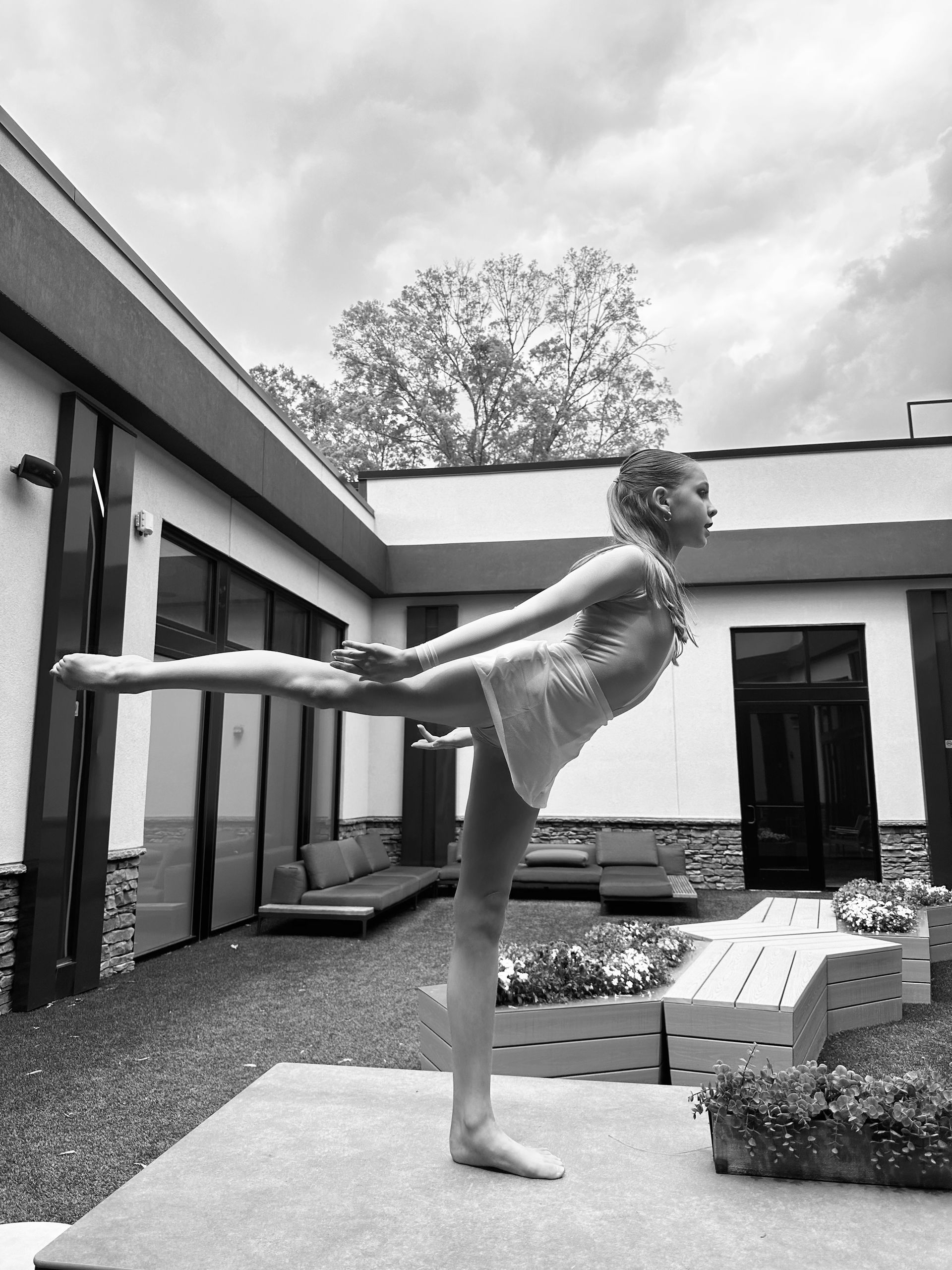 A person in a leotard balances, one leg extended, in an outdoor setting.