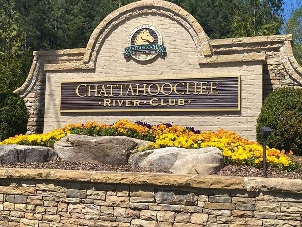 Sign for the Chattahoochee River Club with stone and floral landscaping, sunny day.