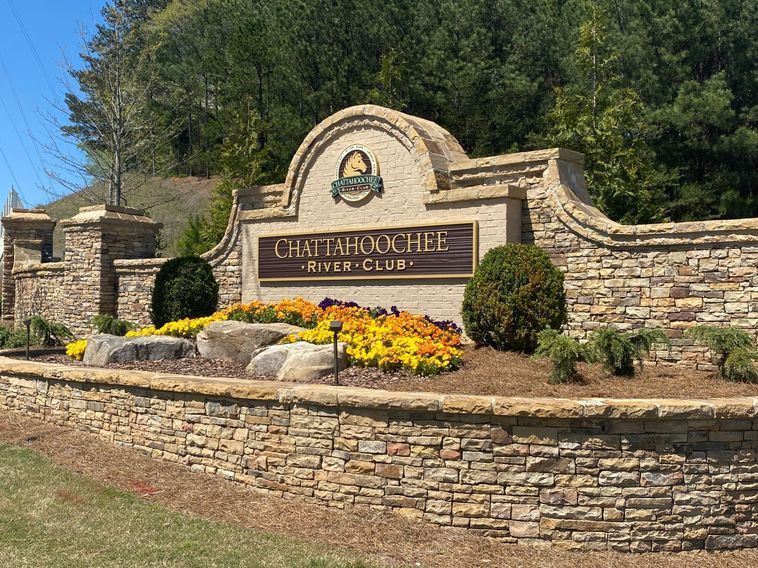 Sign for Chattahoochee River Club with stone wall and flowers.