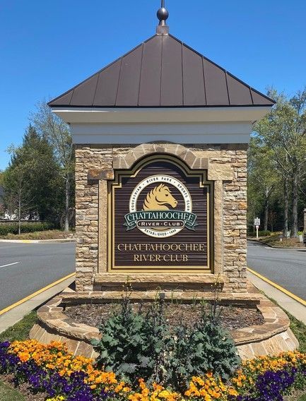 Entrance sign for the University Club of South Carolina, brown and tan stone, with flowerbeds and blue sky.